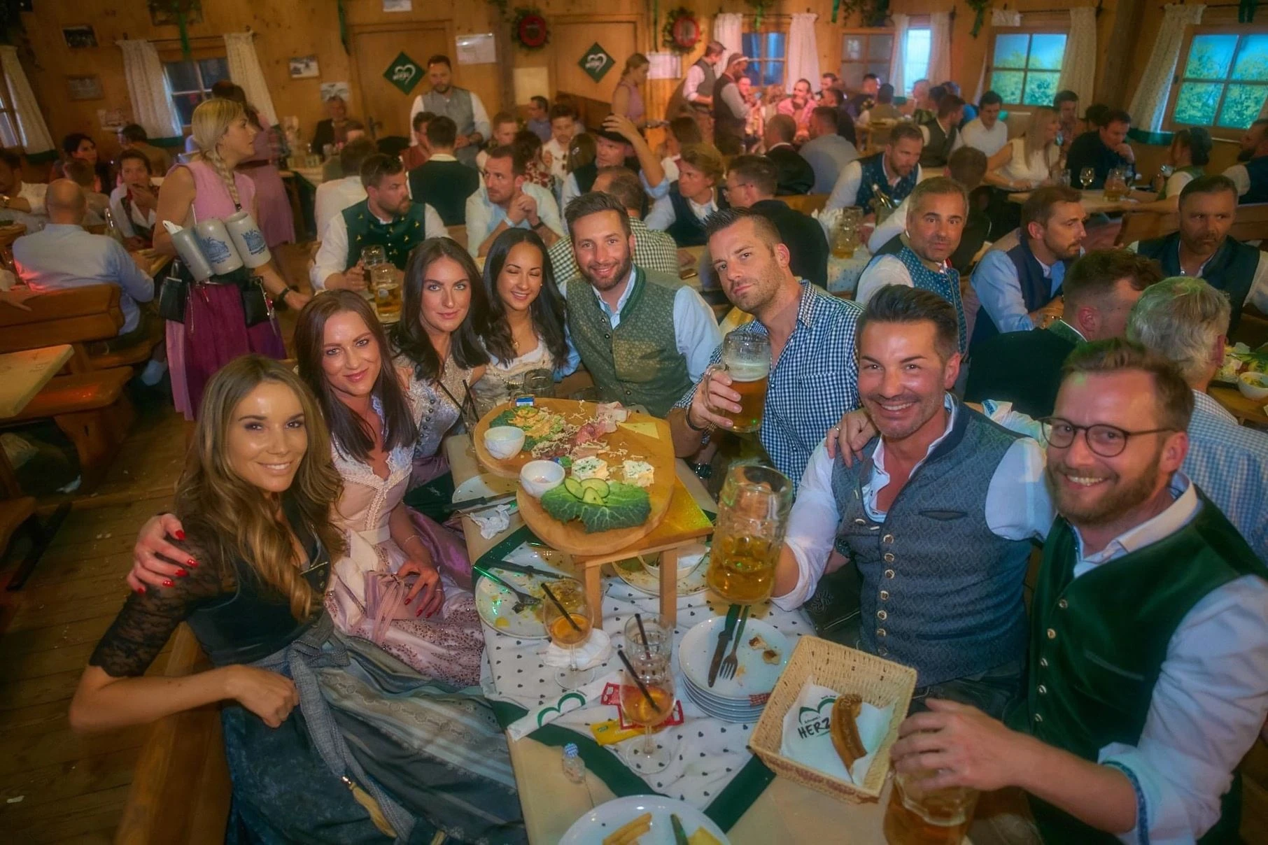 Fröhliche Gruppe in Tracht prostet an einem Biertisch im vollbesetzten Festzelt in die Kamera