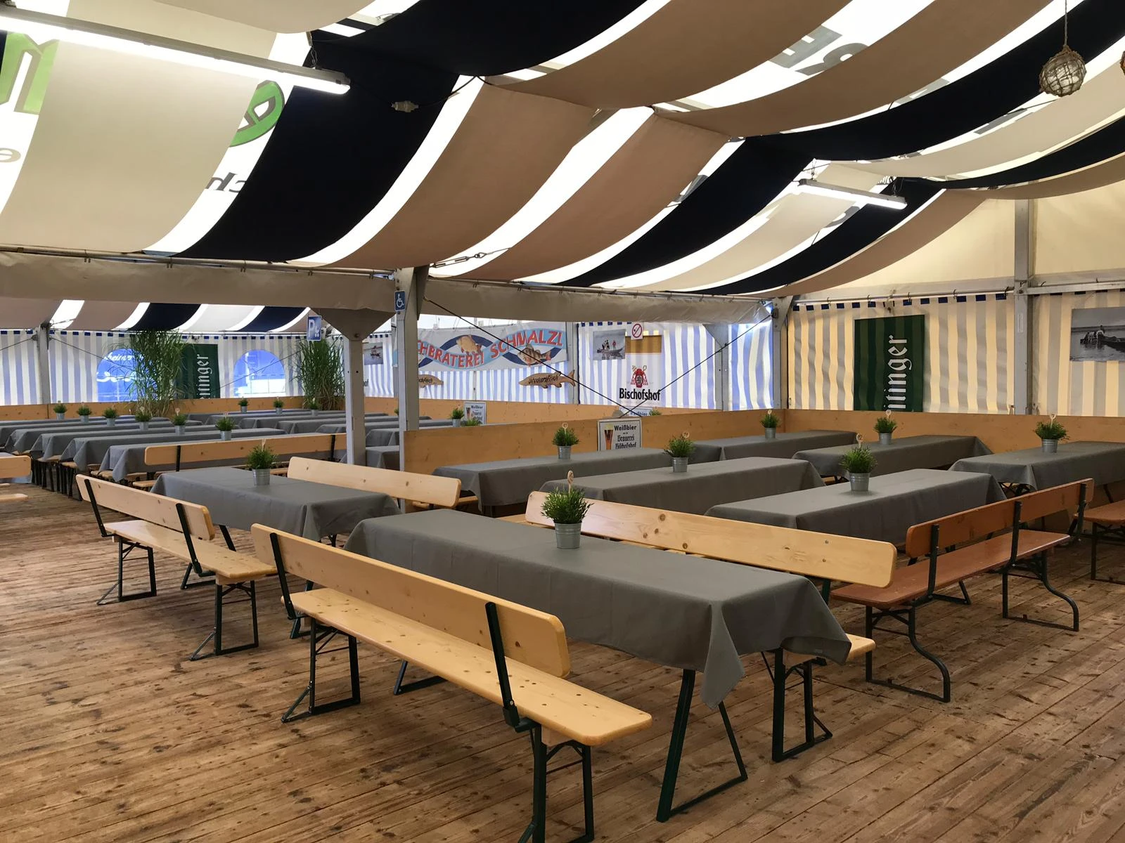 Innenansicht des Festzelts mit langen Biertischen und weiß-schwarzen Deckensegeln
