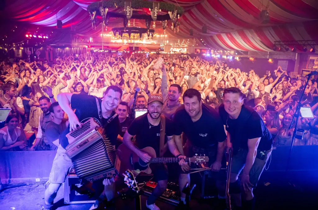 Vier Musiker von Tschamstera spielen auf der Bühne im Festzelt vor jubelndem Publikum, mit Akkordeon und Gitarre