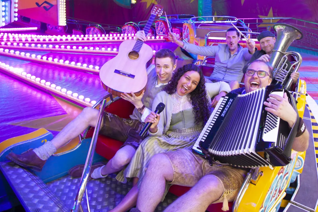 Fünf Musiker der Voigams im bunten Karussell-Setting mit Akkordeon, Gitarre und Tuba, ausgelassen lachend