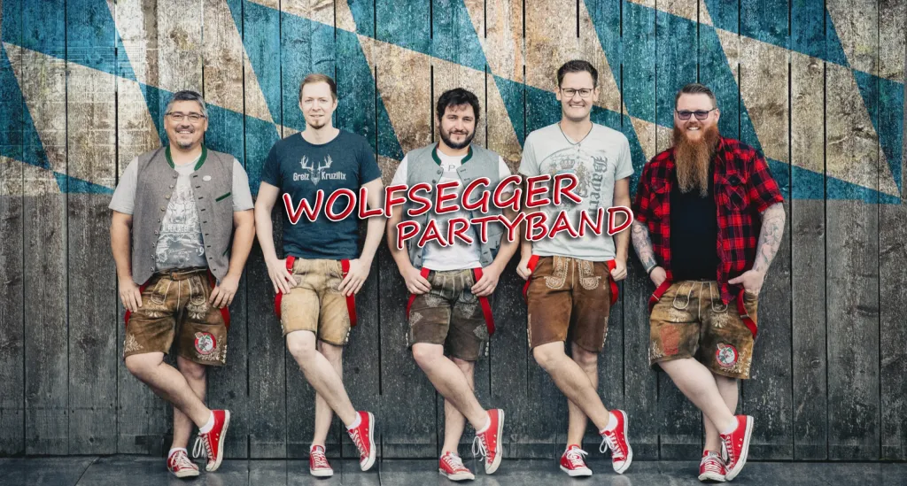 Fünf Musiker der Wolfsegger Partyband in Lederhosen vor blau-weißer Holzwand