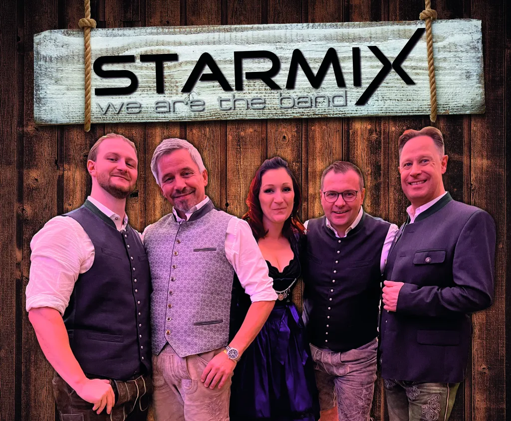 Fünfköpfige Band Starmix in festlicher Kleidung vor einem Holzschild mit Bandnamen