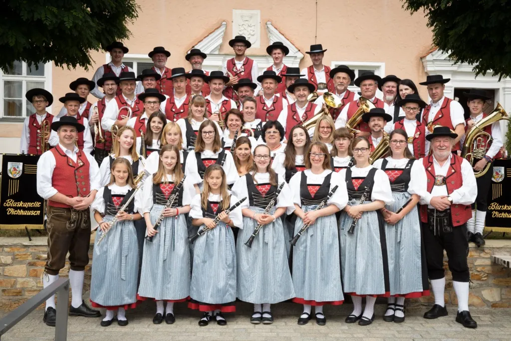 Blaskapelle Viehhausen in roten Trachtenwesten und Dirndln als Gruppenfoto vor einem Gebäude