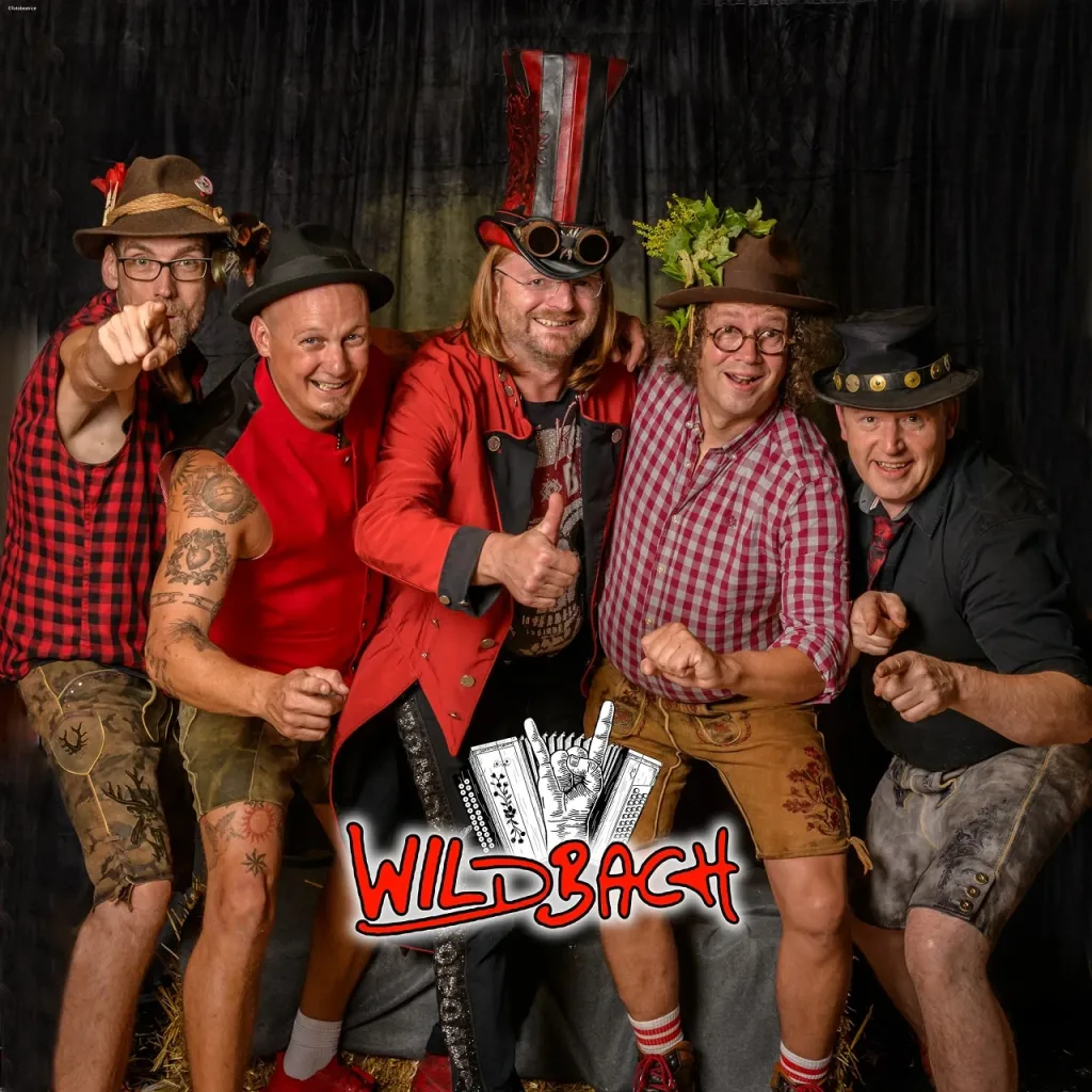 Fünf Musiker der Band Wildbach in Lederhosen mit Hüten posieren vor schwarzem Vorhang