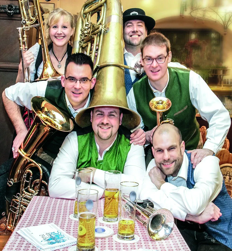 Sechsköpfige Blaskapelle DeFuchsn in grünen Westen am Tisch mit Bierkrügen und Tuba
