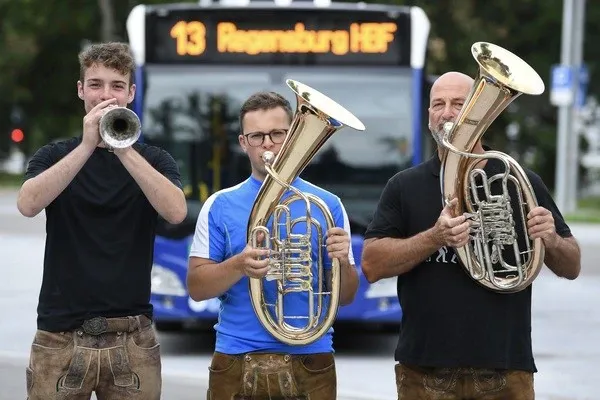 Drei Blasbrothers-Musiker mit Trompete, Tenorhorn und Tuba vor einem Linienbus