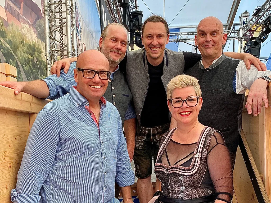 Fünf Bandmitglieder von Erwin und die Heckflossen mit Sängerin Susanne vor Bühnenkulisse im Festzelt