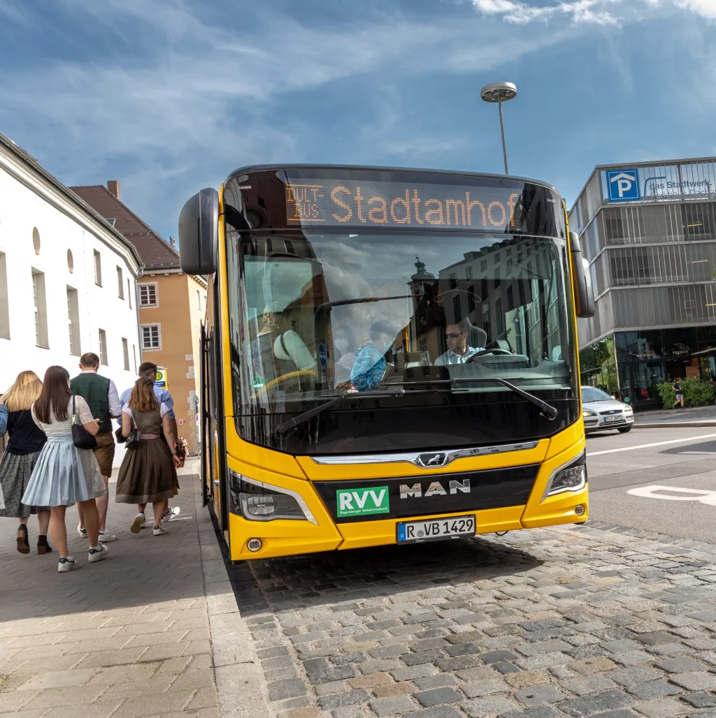Gelber RVV-Linienbus mit Anzeige „Dult-Bus Stadtamhof“, einsteigende Fahrgäste in Tracht