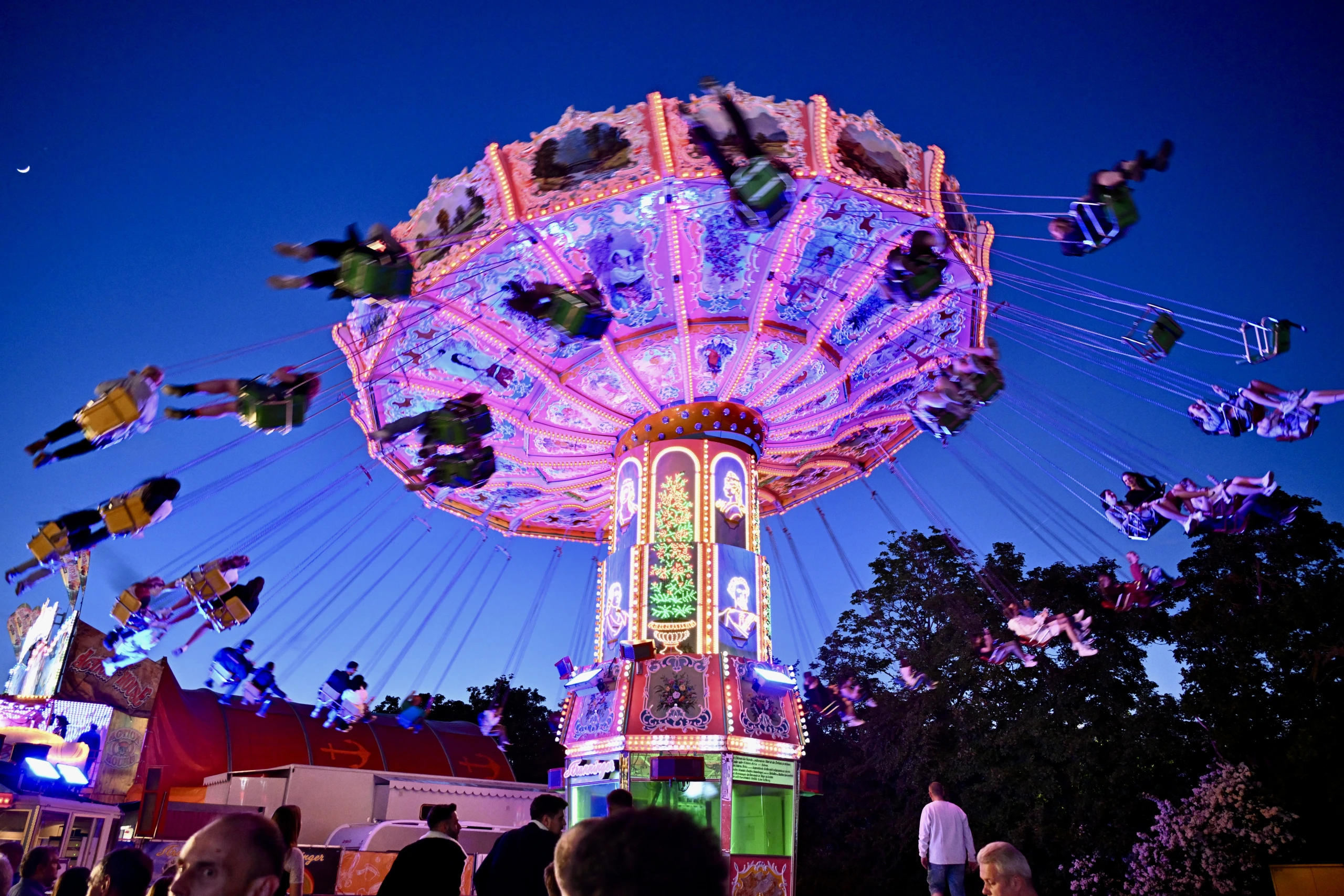 Beleuchtetes Kettenkarussell in voller Fahrt vor blauem Abendhimmel