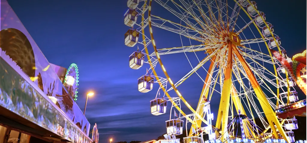 Beleuchtetes Riesenrad und Festbuden im Dultplatz bei Abenddämmerung
