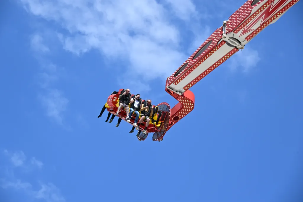 Fahrgäste im Hochfahrgeschäft schweben gesichert vor blauem Himmel