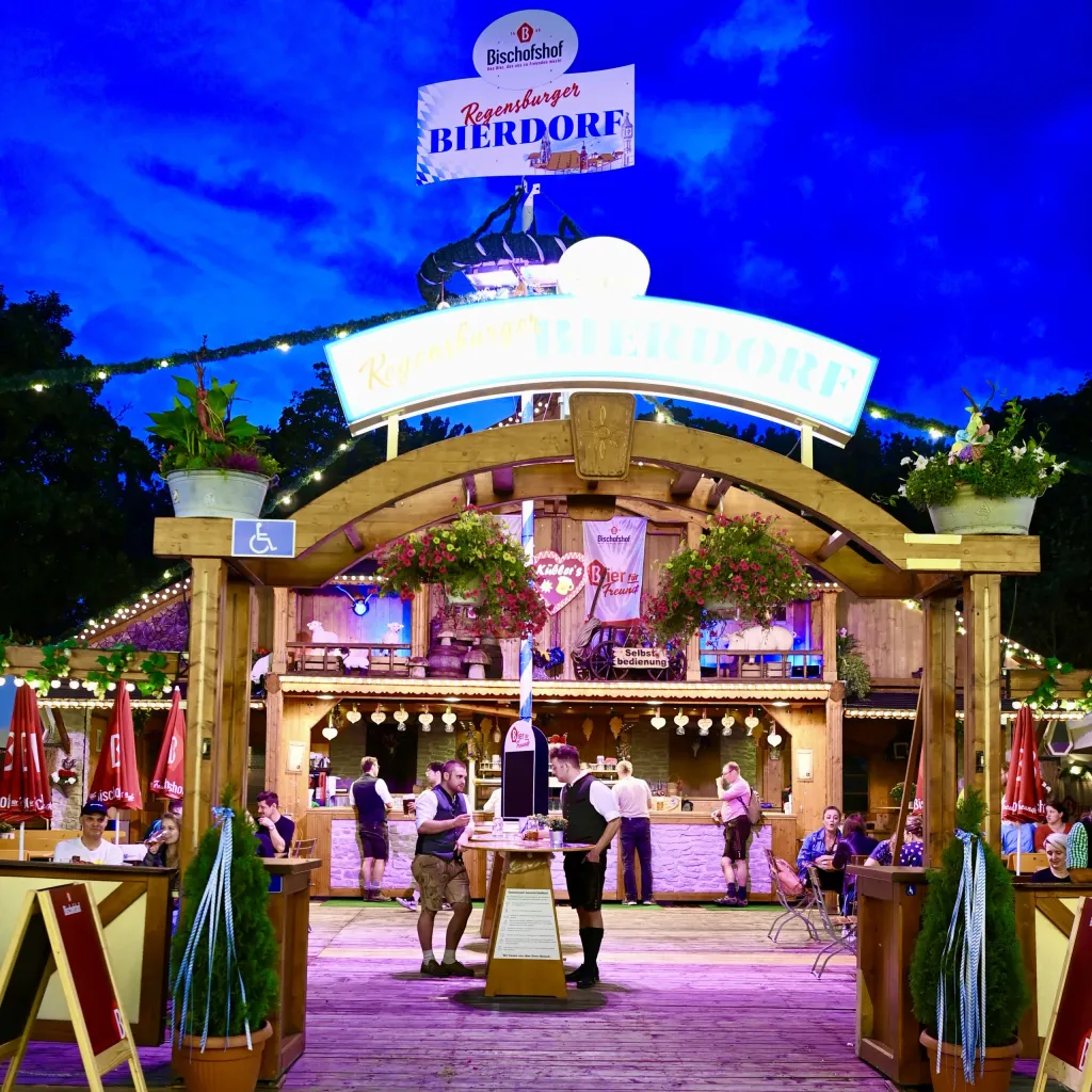 Beleuchteter Holzpavillon des Regensburger Bierdorfs mit Bedienung in der Dämmerung