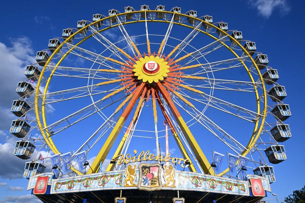 Buntes Riesenrad mit gelber Nabe und bayerischem Wappen vor blauem Himmel