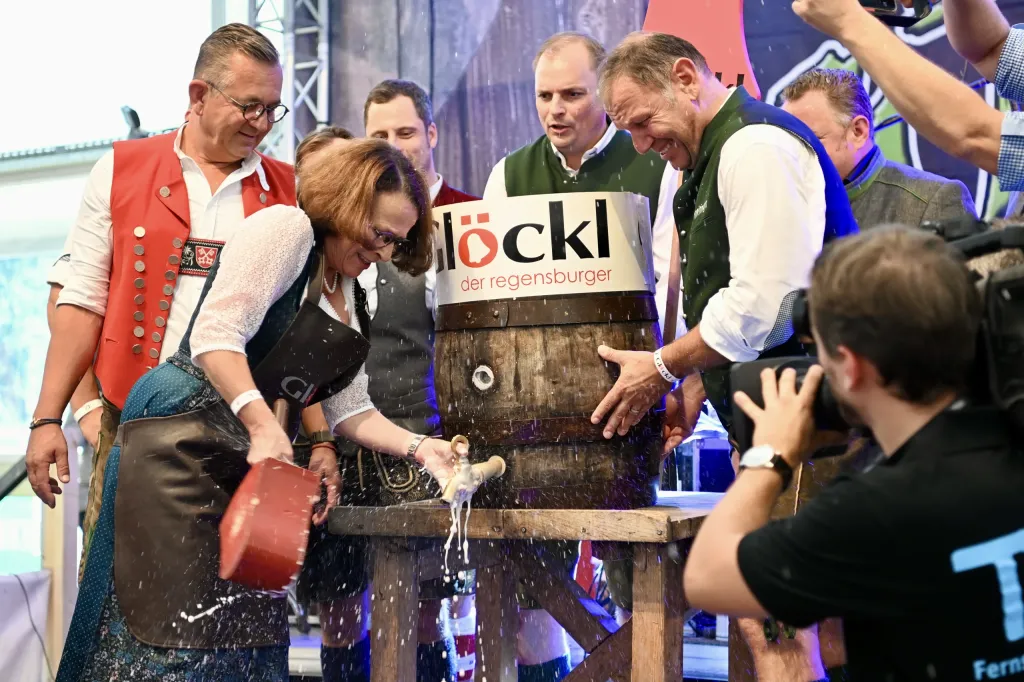 Bieranstich am Glöckl-Festzelt: Frau in Tracht schlägt den Zapfhahn ins Holzfass, Männer schauen zu