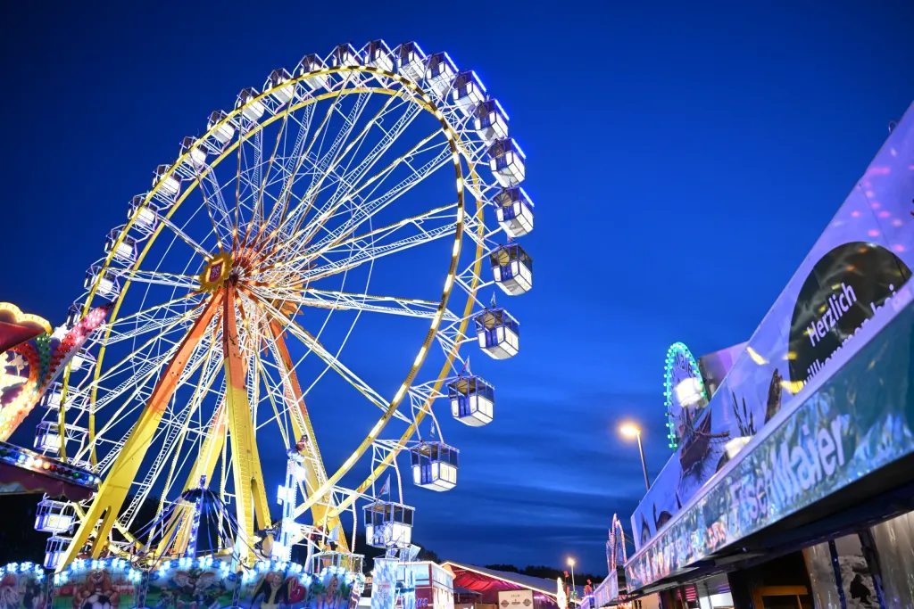 Beleuchtetes Riesenrad zur blauen Stunde mit Verkaufsbuden im Vordergrund