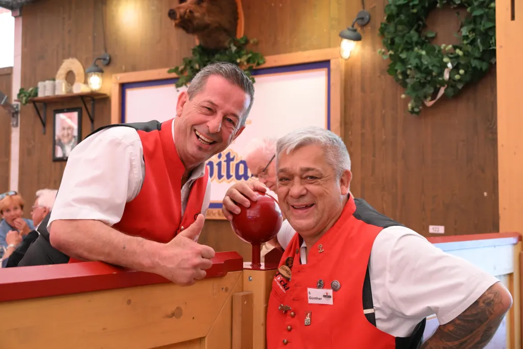 Zwei lachende Festzeltordner in roten Westen lehnen am Holzgeländer im Festzelt