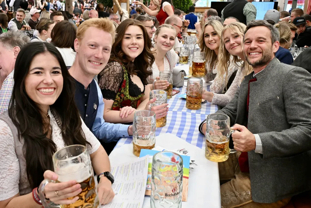 Fröhliche Tischrunde im Festzelt prostet mit Maßkrügen in die Kamera
