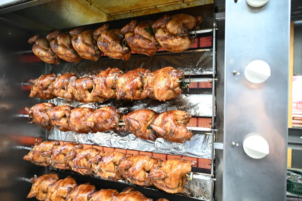 Mehrere Reihen knuspriger Brathähnchen auf Drehspießen am Hähnchengrill