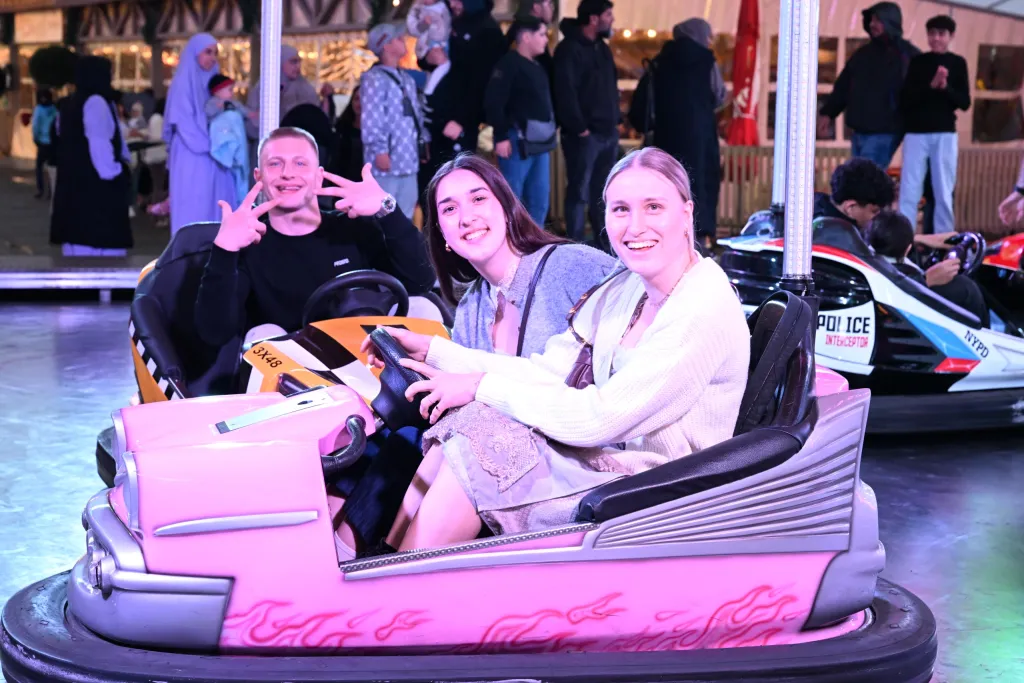 Drei junge Besucher lachen im rosa Autoscooter-Wagen vor einem Polizei-Auto