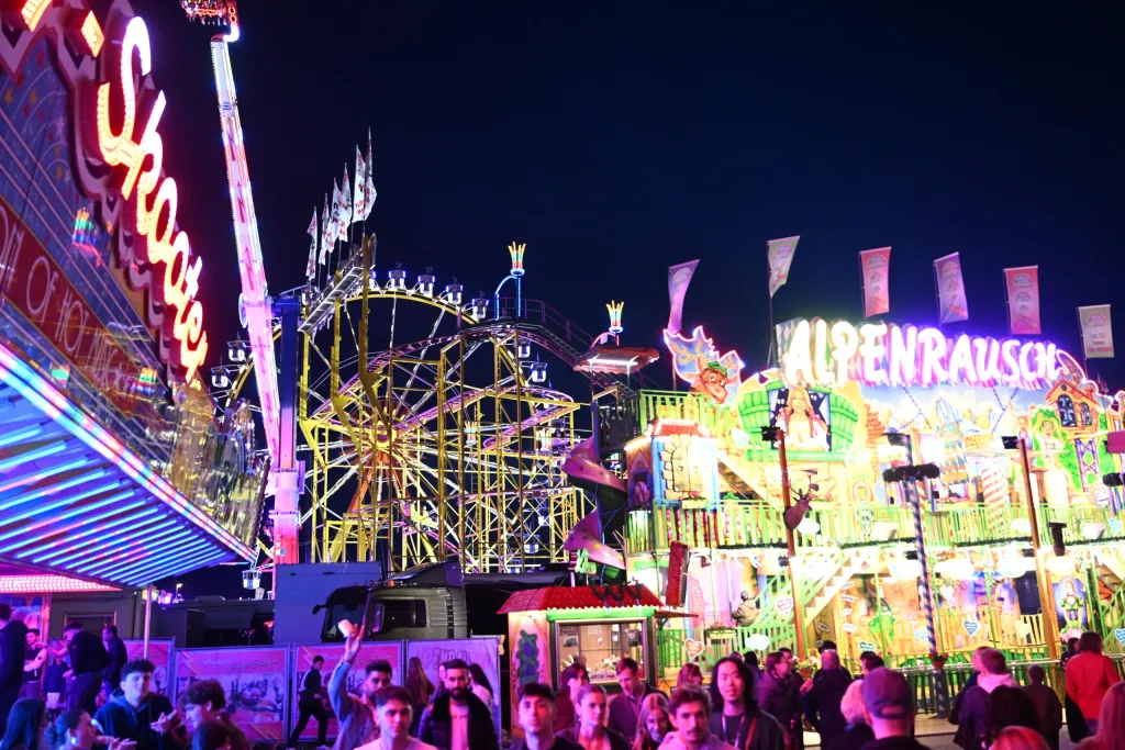 Bunt beleuchtete Achterbahn und Alpenrausch-Fahrgeschäft in der Festplatznacht
