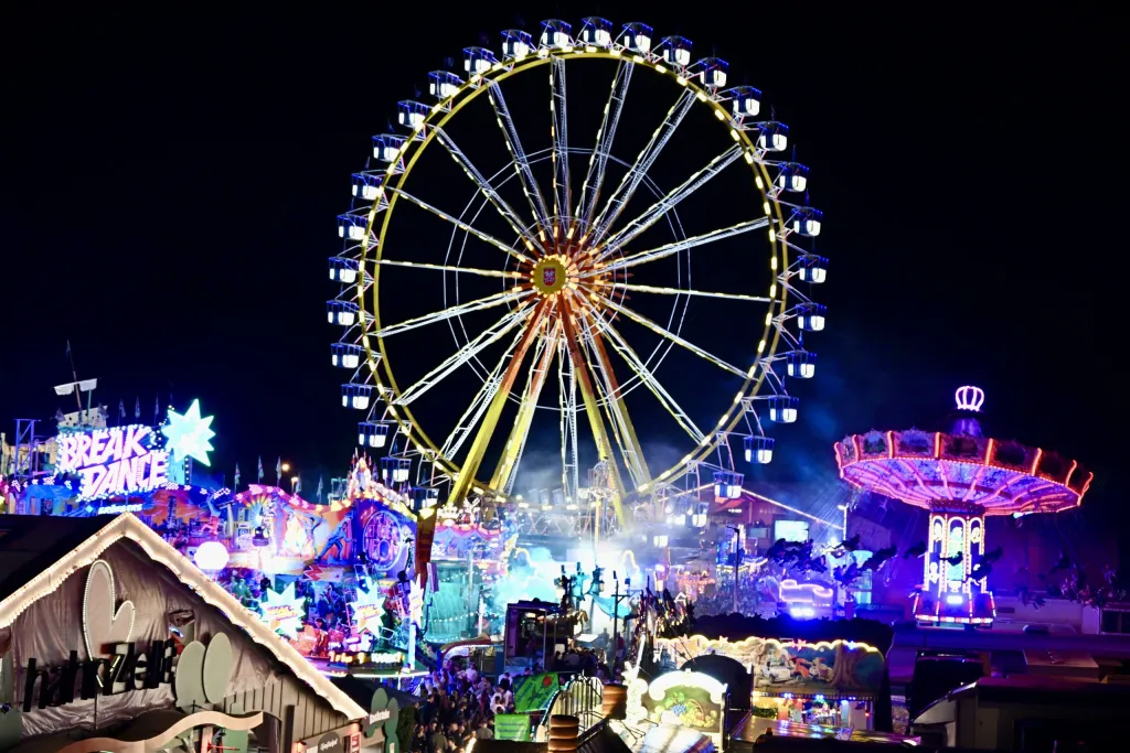Beleuchtetes Riesenrad und Fahrgeschäfte der Dult in bunter Nachtbeleuchtung