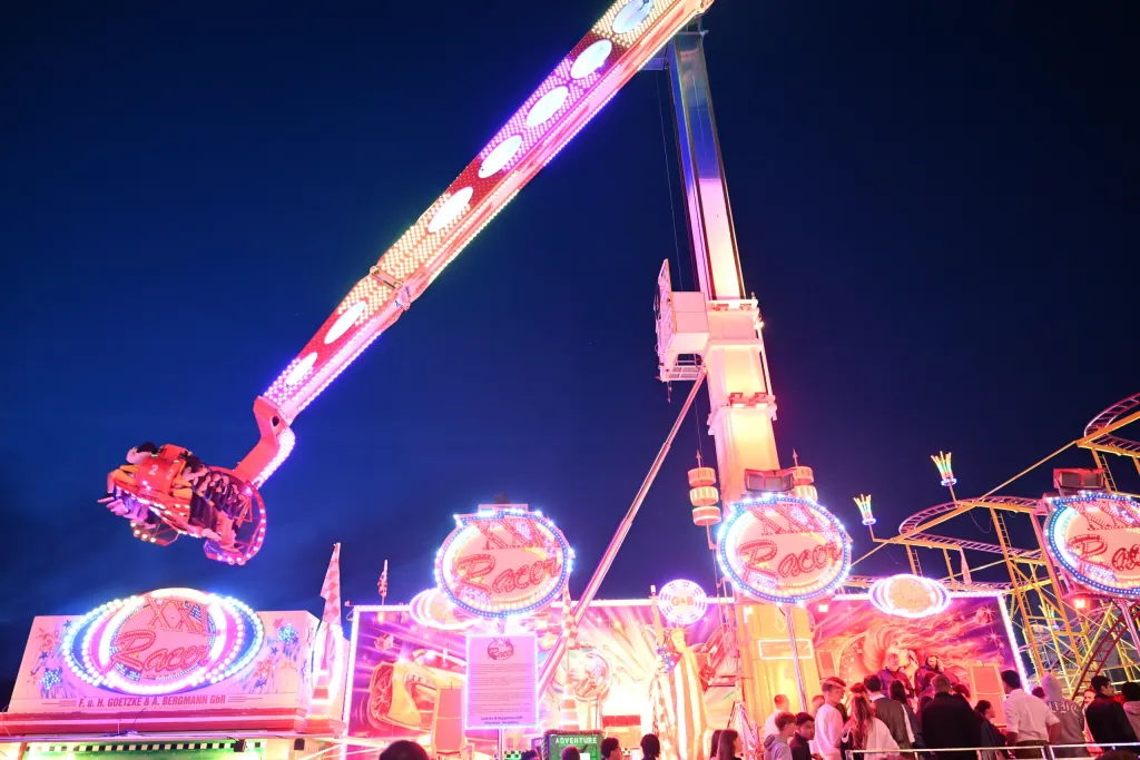 Pink beleuchtetes Fahrgeschäft Race bei Nacht auf der Dult mit Schaulustigen