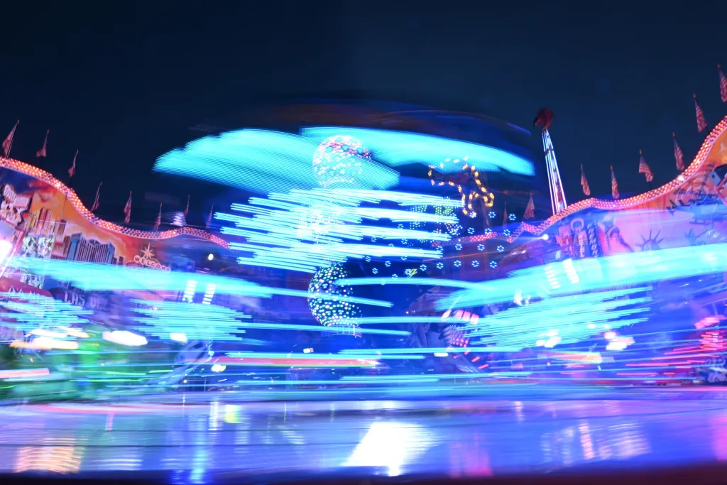 Bewegungsunscharfes Karussell mit Lichtspuren in Blau und Pink bei Nacht