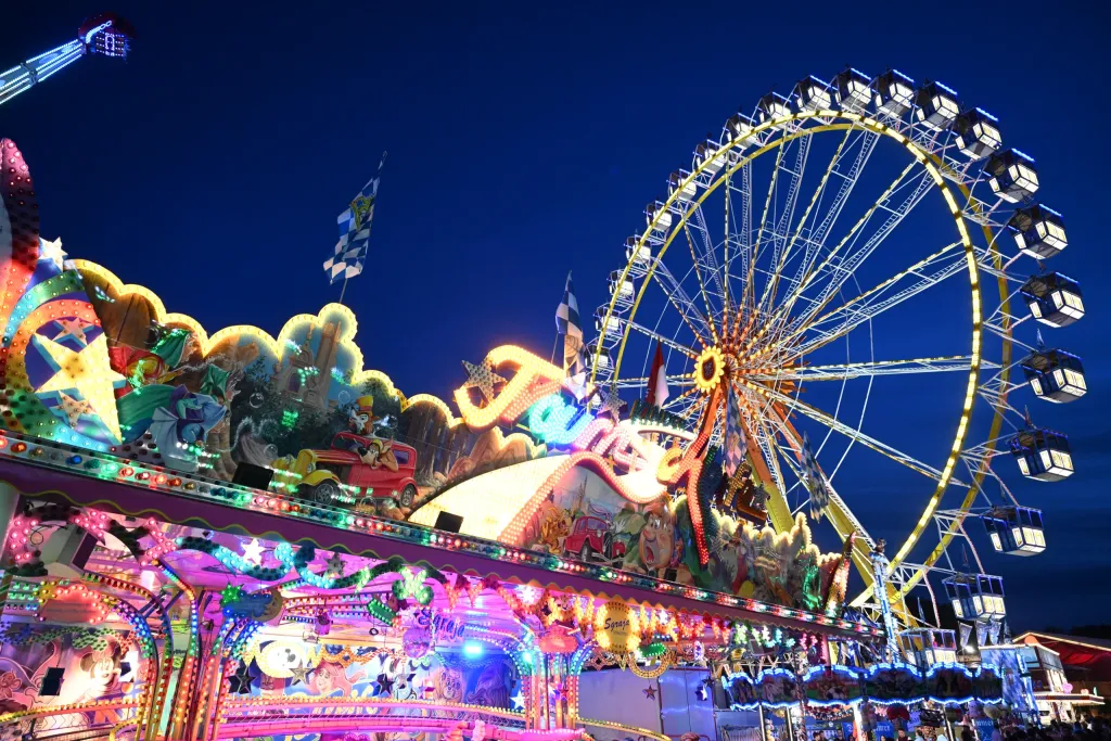 Beleuchtete Fahrgeschäfte und Riesenrad in der blauen Stunde am Festplatz
