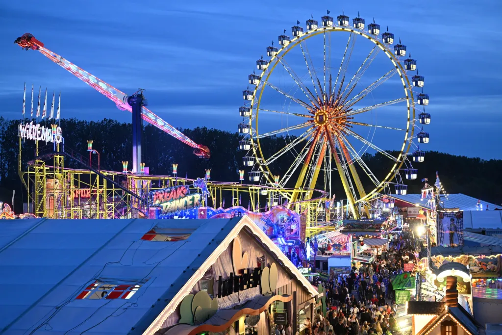 Beleuchtetes Riesenrad und Fahrgeschäfte auf dem Dultplatz in der Abenddämmerung