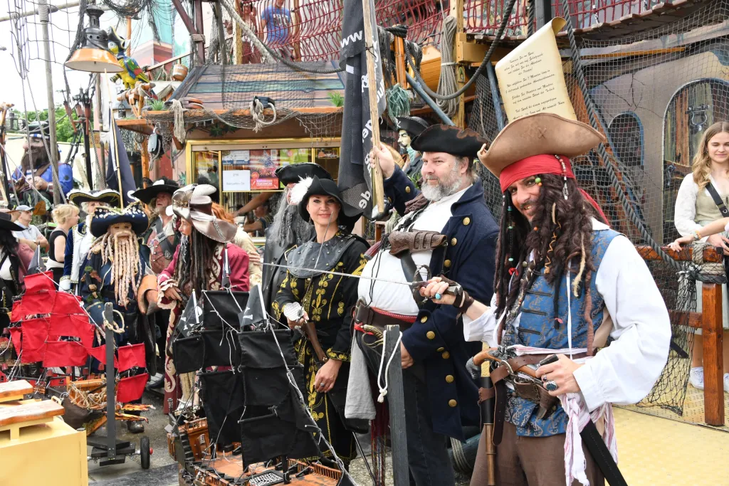 Als Piraten verkleidete Schausteller posieren vor einem Piratenschiff-Fahrgeschäft auf der Dult