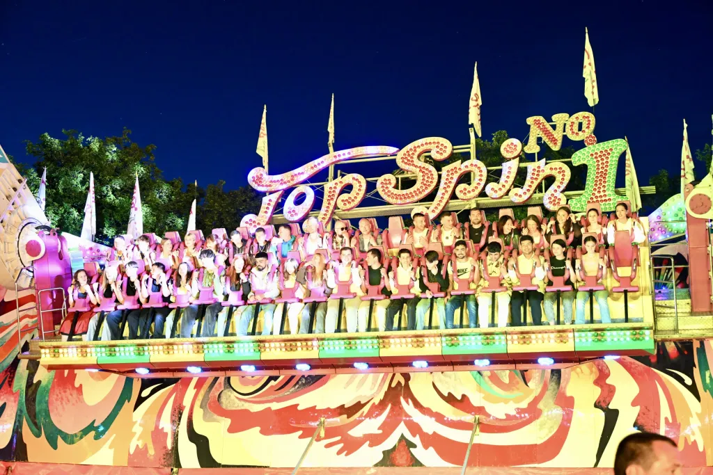 Bunt beleuchtete Top Spin-Schaukel bei Nacht mit Fahrgästen in den Sitzen