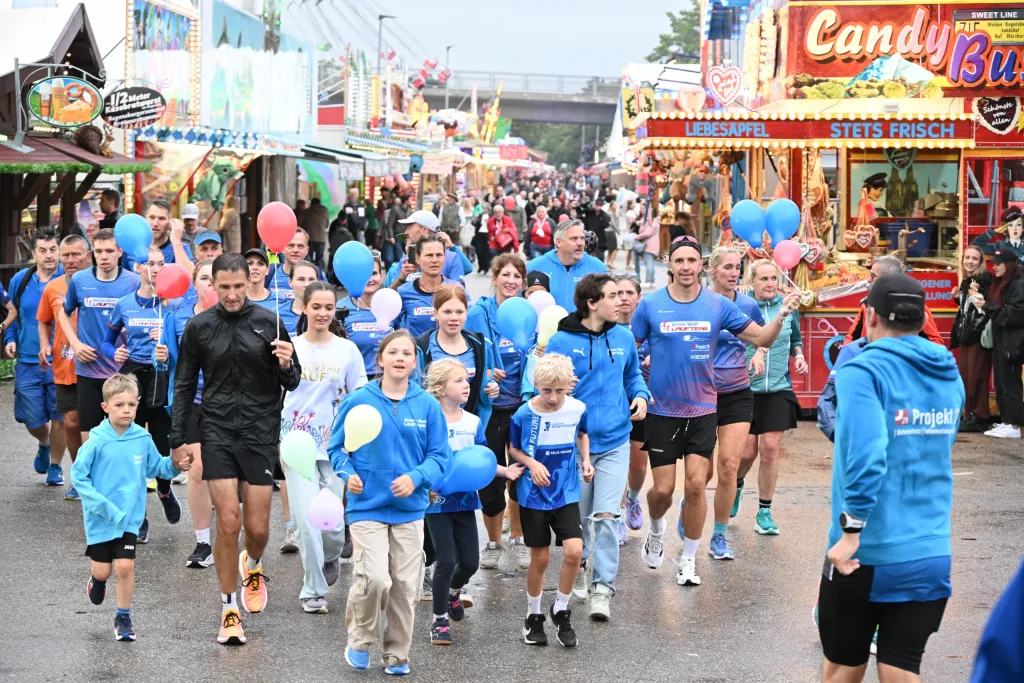 Teilnehmer in blauen Shirts beim Spendenlauf zwischen Festbuden auf der Herbstdult