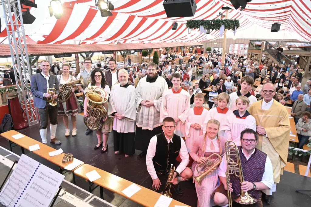 Geistliche und Blasmusiker in Tracht auf der Festzeltbühne vor vollem Publikum beim Gottesdienst