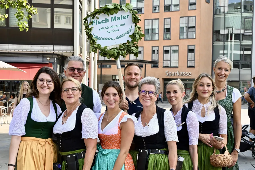 Mitarbeiterinnen von Fisch Maier in Dirndln vor einem Schild zum 50-jährigen Dult-Jubiläum