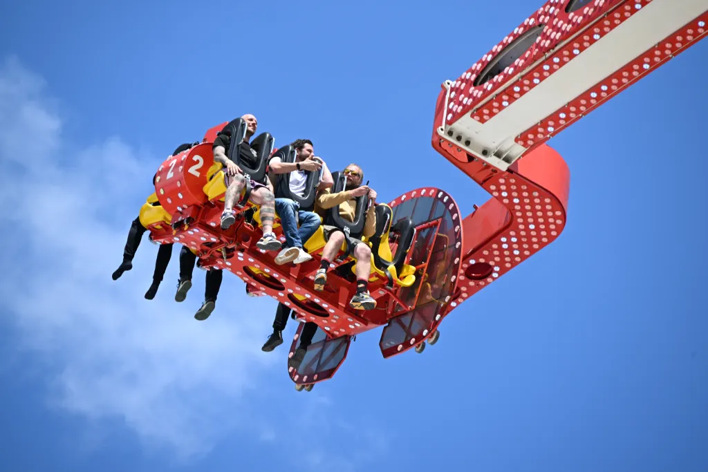 Fahrgäste hängen an Sitzen des Hangover-Loopings vor blauem Himmel