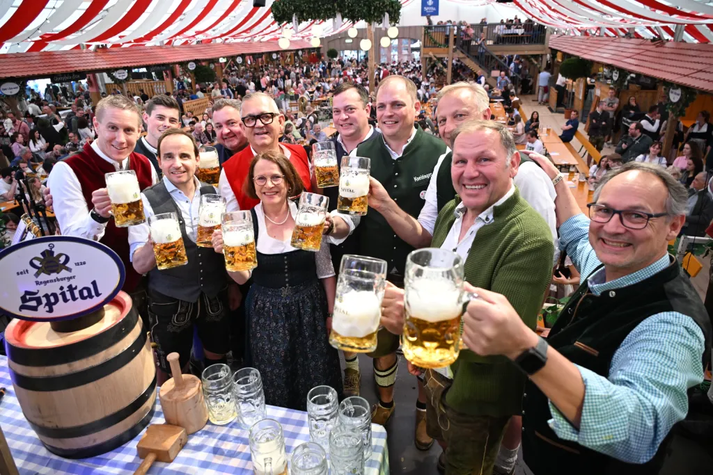 Festliche Runde in Tracht stößt mit Maßkrügen am Spital-Bierfass im Festzelt an