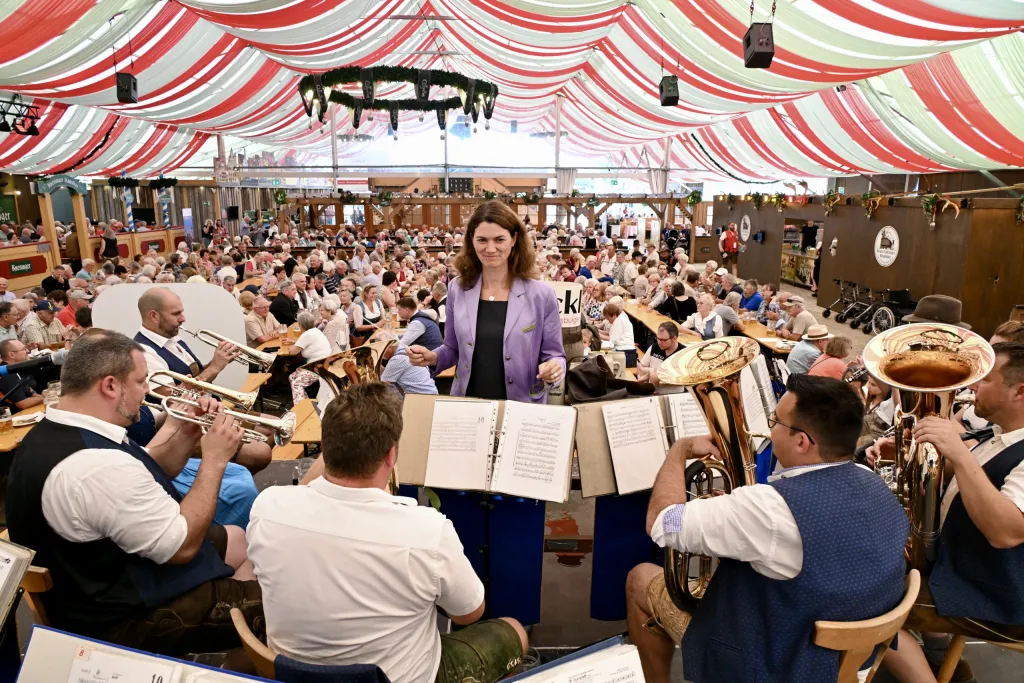Blaskapelle in Tracht und Dirigentin unter dem rot-weißen Festzeltdach beim Konzert