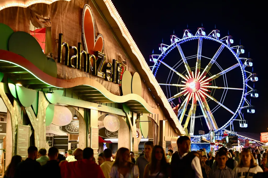 Beleuchtetes Hahn Zelt mit Logo und Riesenrad im Hintergrund bei Nacht