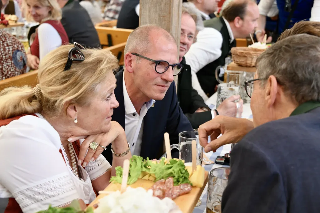 Festzeltgäste in Tracht im Gespräch an Tisch mit Brotzeitbrettl