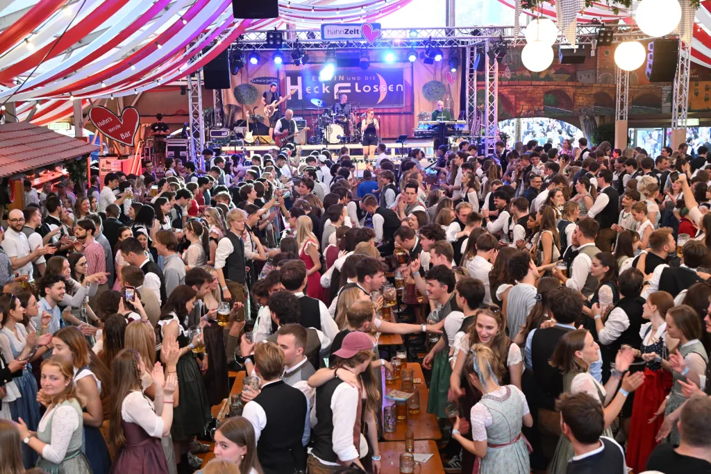 Tanzendes Publikum in Tracht im Hahn Zelt vor der beleuchteten Bühne der Band Heckflossen, rot-weißes Dach
