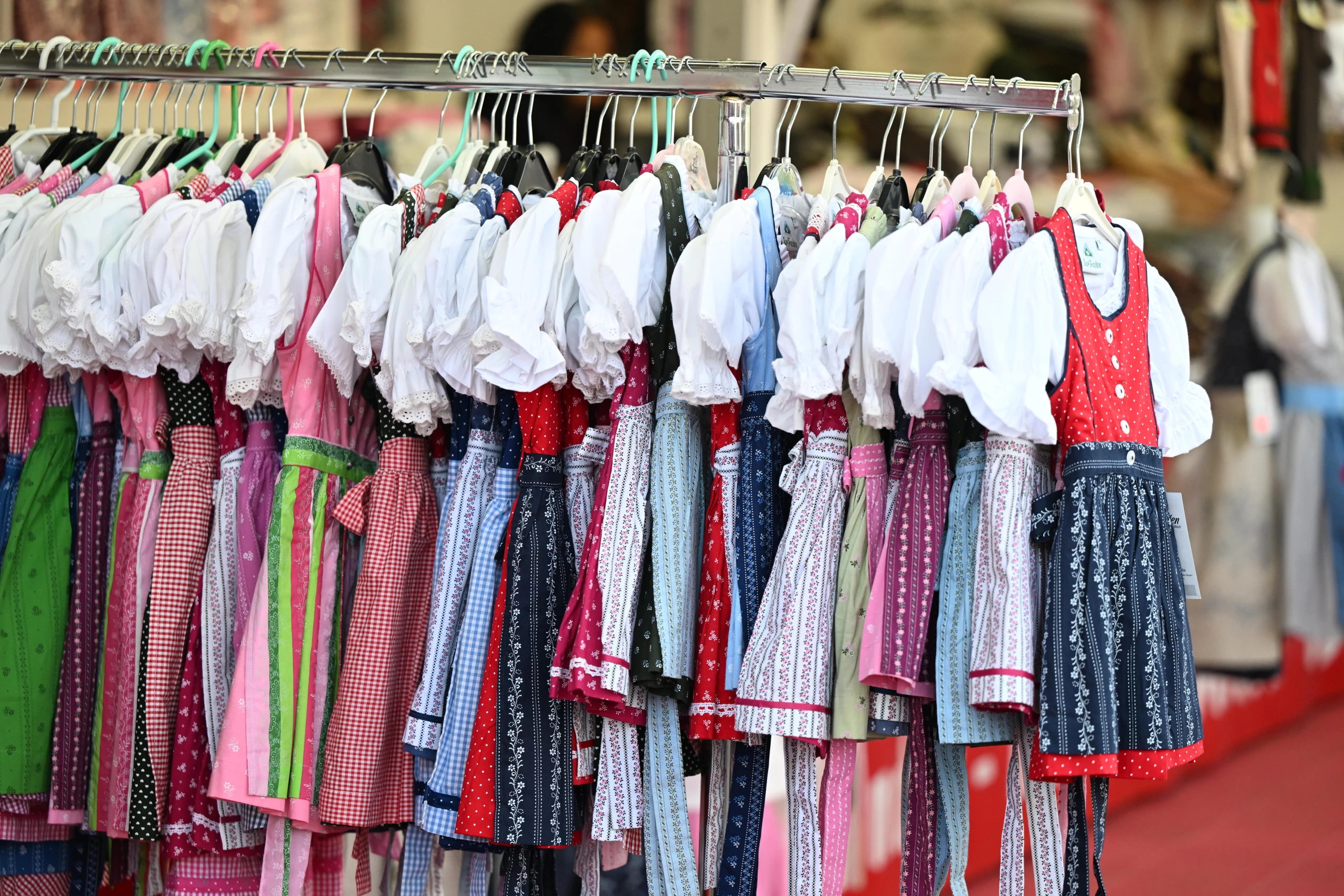 Bunte Dirndl in Reihen auf Kleiderbügeln am Verkaufsstand der Dult