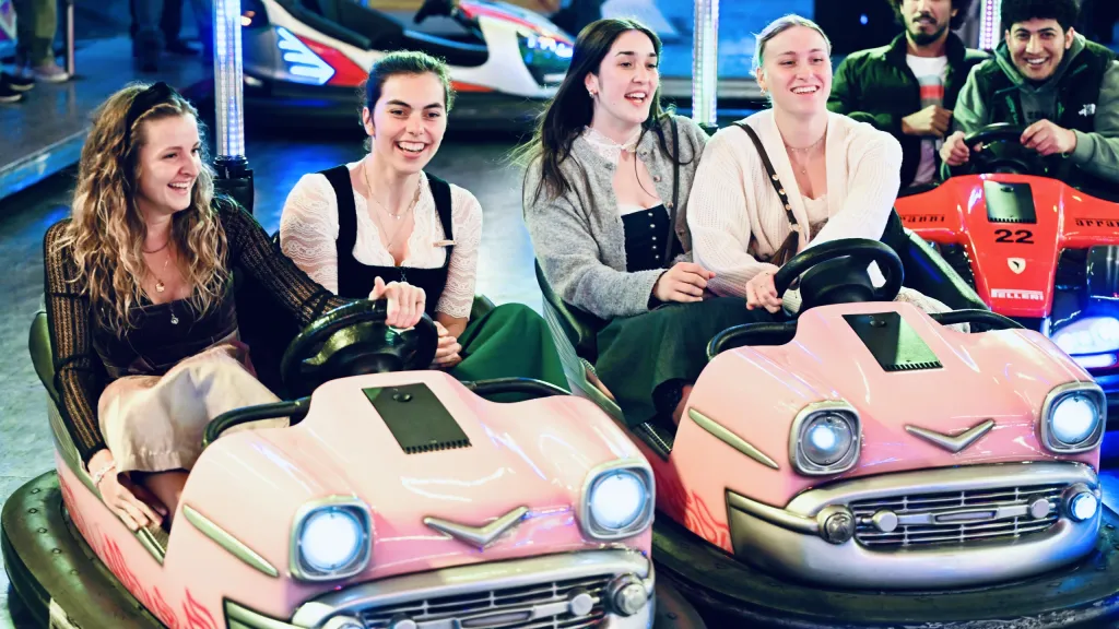 Junge Frauen lachen in rosafarbenen Autoscootern über die Schulter