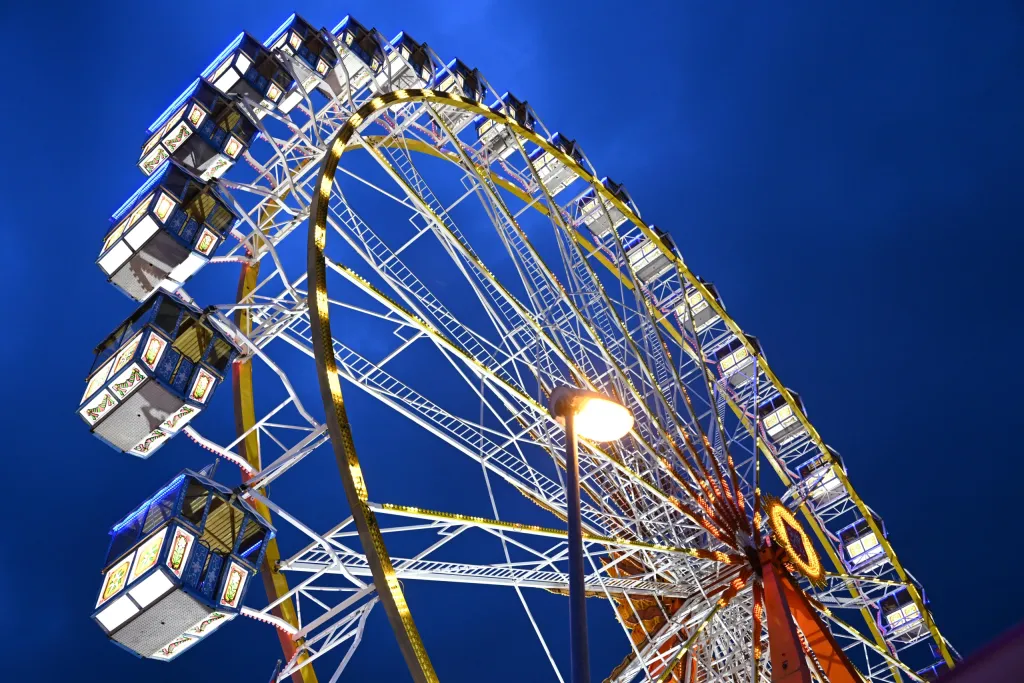 Beleuchtetes Riesenrad mit gelben Streben und Straßenlaterne vor blauem Nachthimmel