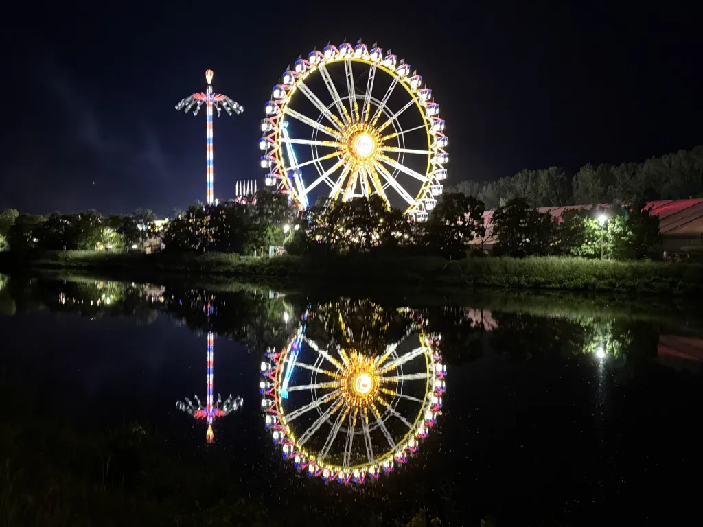 Beleuchtetes Riesenrad und Kettenkarussell der Dult bei Nacht, gespiegelt in der Donau