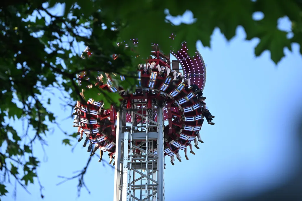 Kirmes-Fahrgeschäft mit rotierenden Gondelringen hoch in der Luft, gerahmt von Baumästen vor Abendhimmel