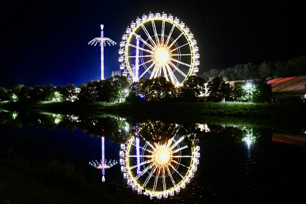 Beleuchtetes Riesenrad spiegelt sich nachts im ruhigen Wasser des Donaukanals