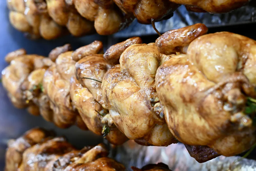 Goldbraune Brathähnchen drehen sich am Spieß über dem Grillfeuer