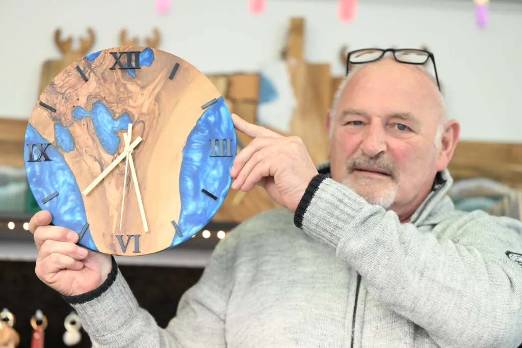 Älterer Mann präsentiert handgefertigte Holzuhr mit blauem Epoxidharz am Stand