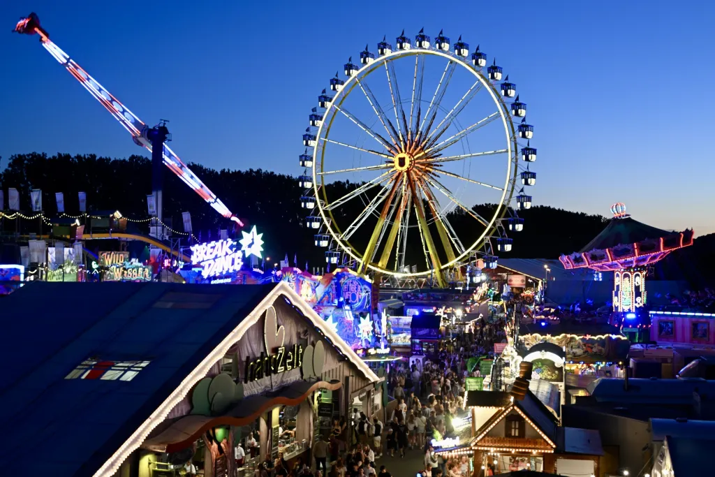 Abendpanorama der Maidult mit beleuchtetem Riesenrad und Fahrgeschäften aus der Vogelperspektive