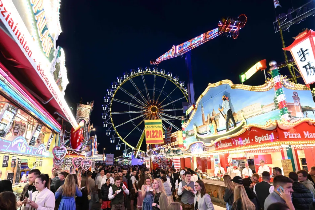 Beleuchtete Vergnügungsmeile der Dult bei Nacht mit Riesenrad, Fahrgeschäften und Besuchermenge